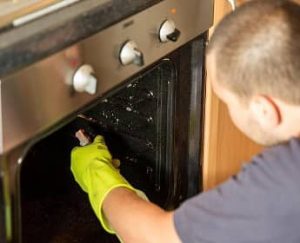 a cleaner spraying an oven with detergent